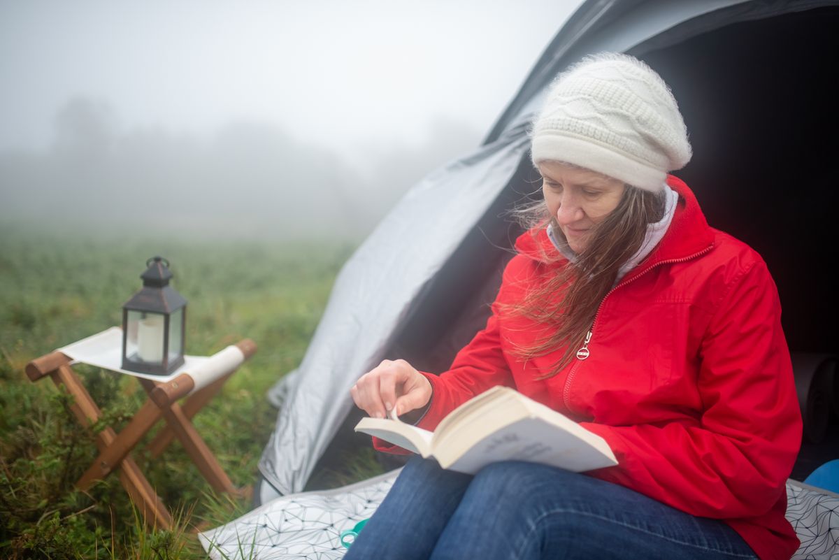 A woman enjoys reading outside her tent in a foggy meadow, embracing a tranquil camping experience.