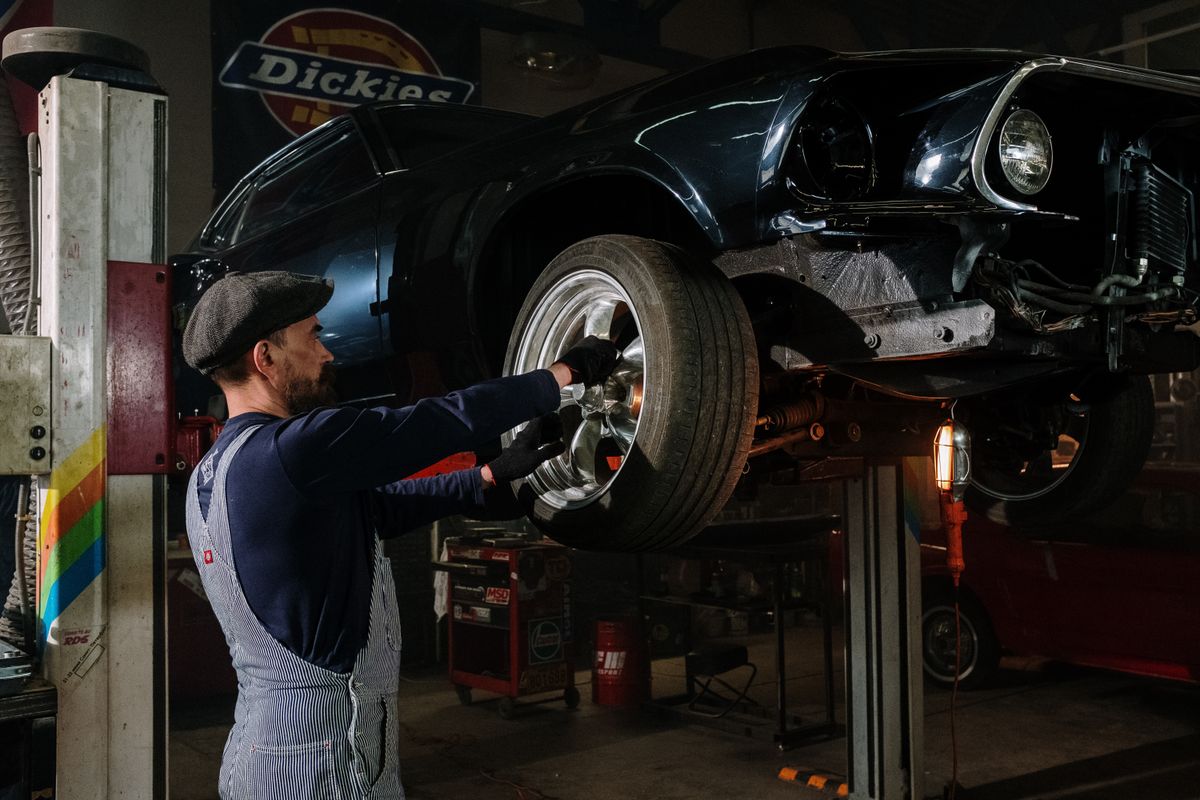 A focused mechanic works on a car wheel in a dimly lit garage, showcasing automotive repair skills.