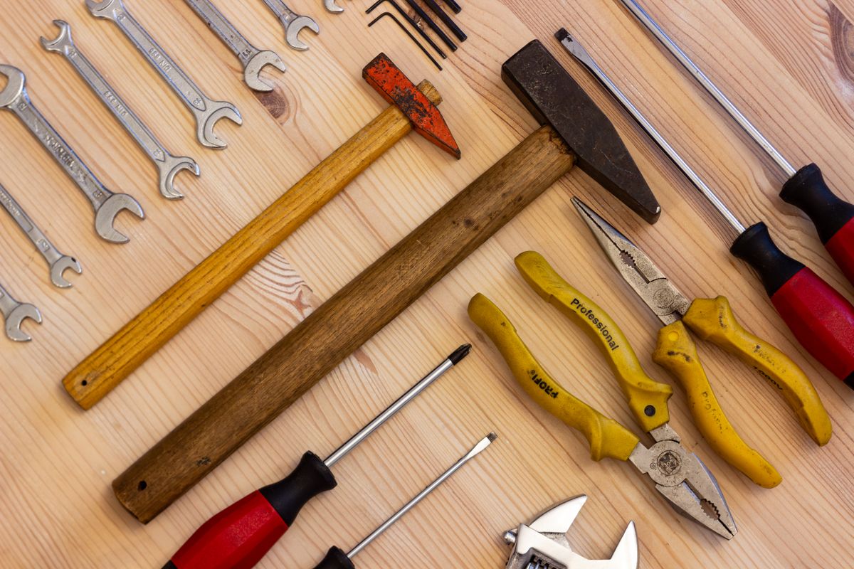 A variety of hand tools including wrenches, screwdrivers, and pliers on a wooden surface.