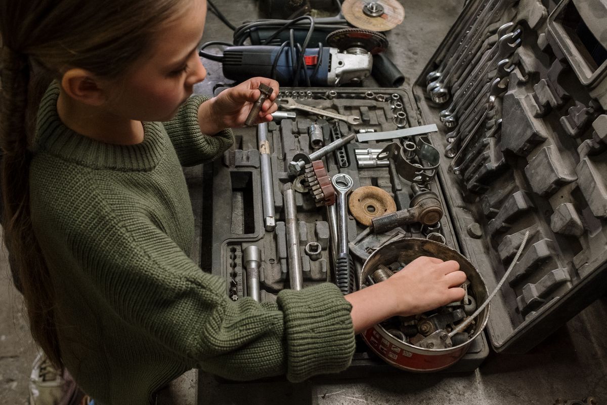 A young girl examines assorted tools and equipment in a garage workshop, depicting curiosity and hands-on learning.