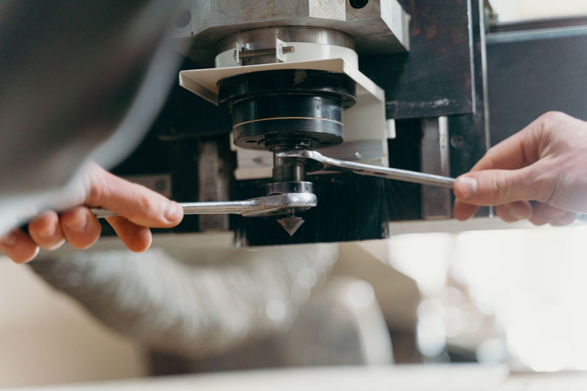 Close-up of hands adjusting a CNC machine using wrenches in an industrial setting.