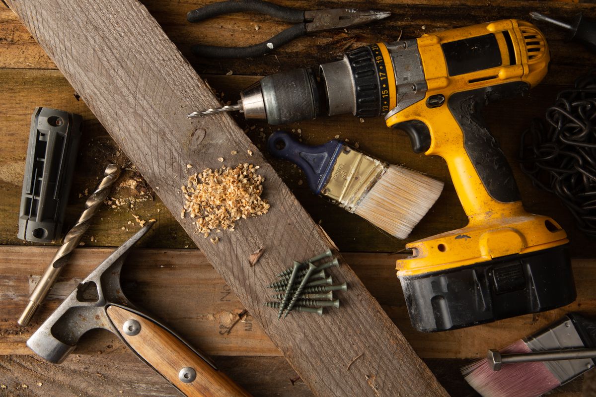 A close-up of various tools including a drill, hammer, and paintbrush on a wooden workbench.