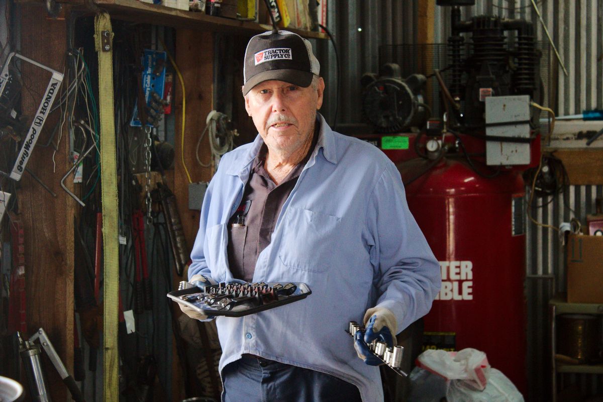 Portrait of an older mechanic holding tools inside a workshop setting, surrounded by equipment.