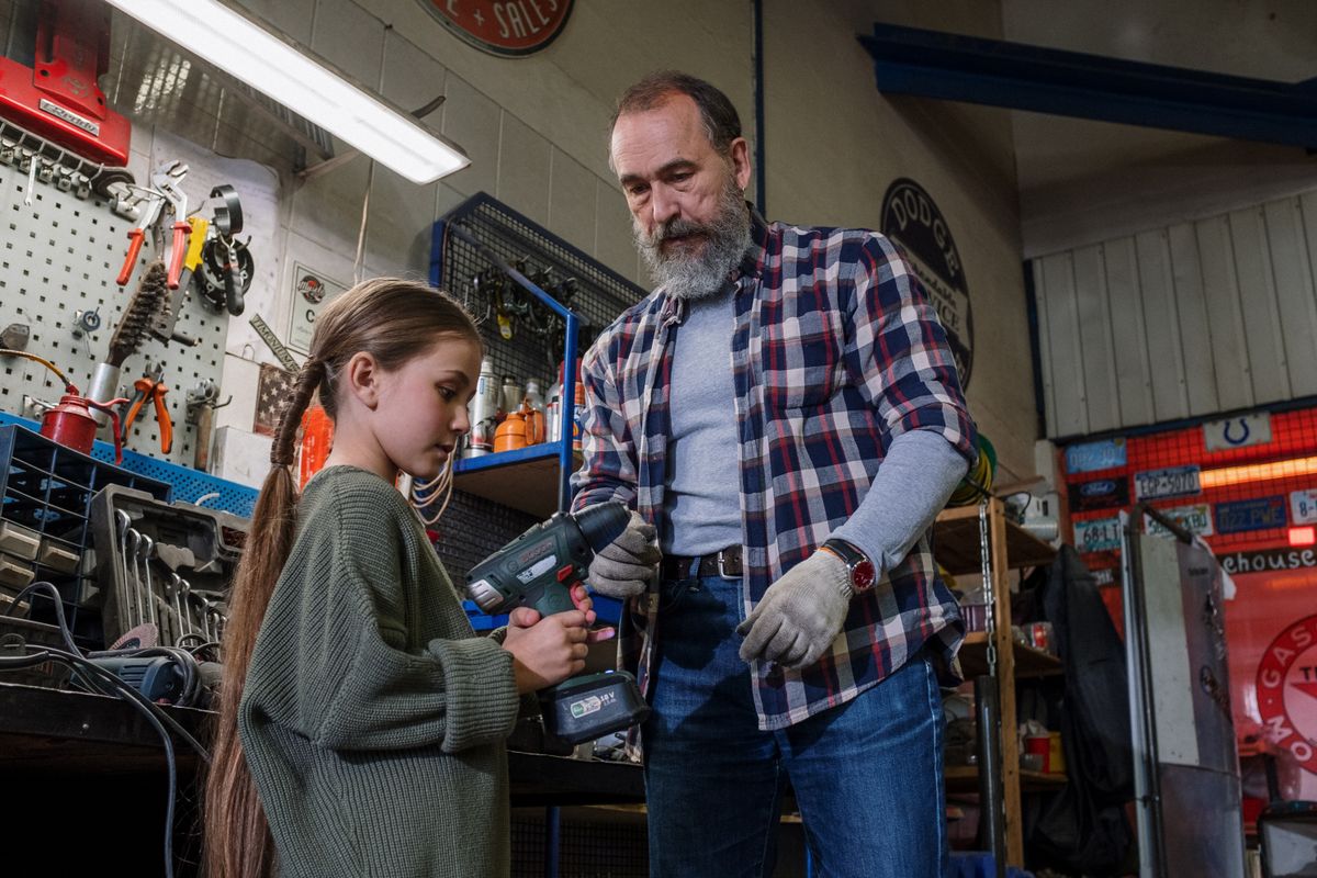 Father and daughter share bonding time in an auto workshop, using power tools.