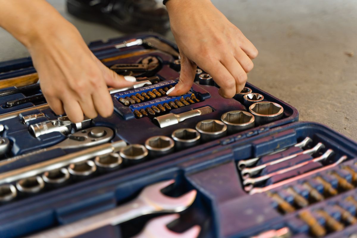 Hands selecting tools from a well-organized toolbox on a concrete surface.