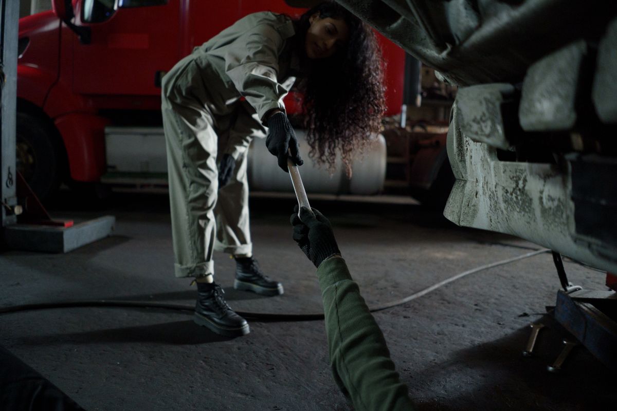 A mechanic handing a wrench in a dimly lit garage workshop, showing teamwork in auto repair.