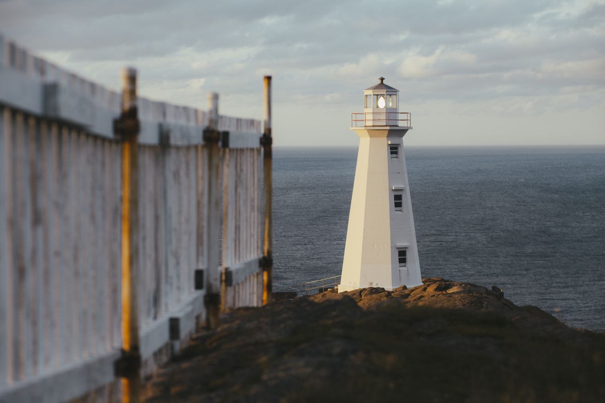 Scenic view of a lighthouse by the ocean with a wooden fence in the foreground at dusk.