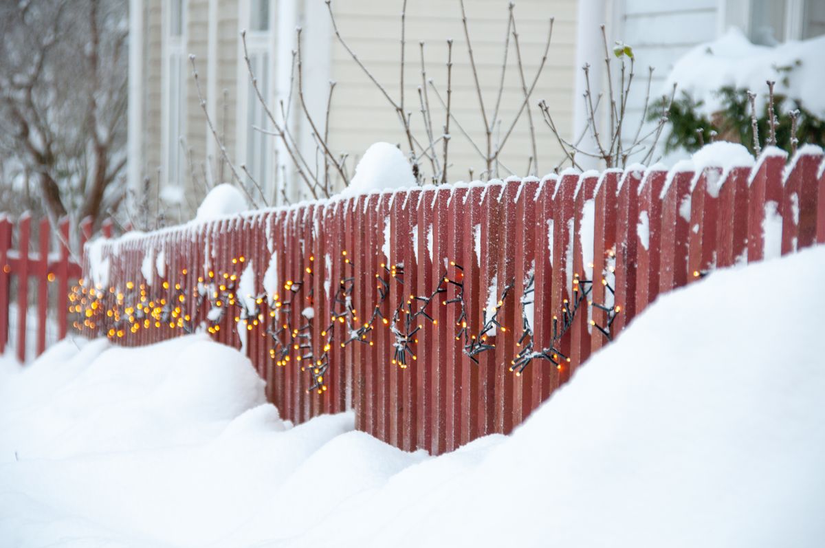 A snowy wooden fence in Finland adorned with warm festive lights reflecting a cozy winter scene.