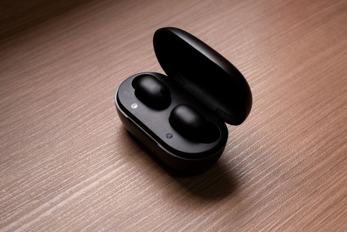 Stylish black wireless earbuds displayed in an open charging case atop a wooden table.