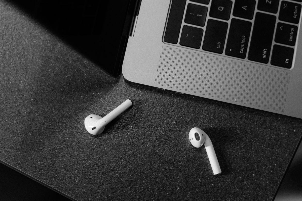 Black and white image of wireless earbuds and laptop, top view.