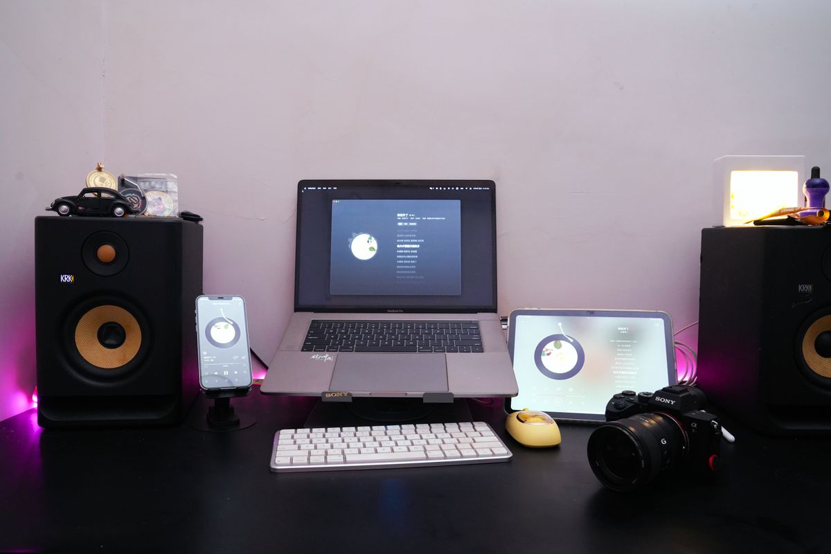 A neat and modern workspace setup featuring a laptop, smartphone, tablet, and audio equipment for music production.