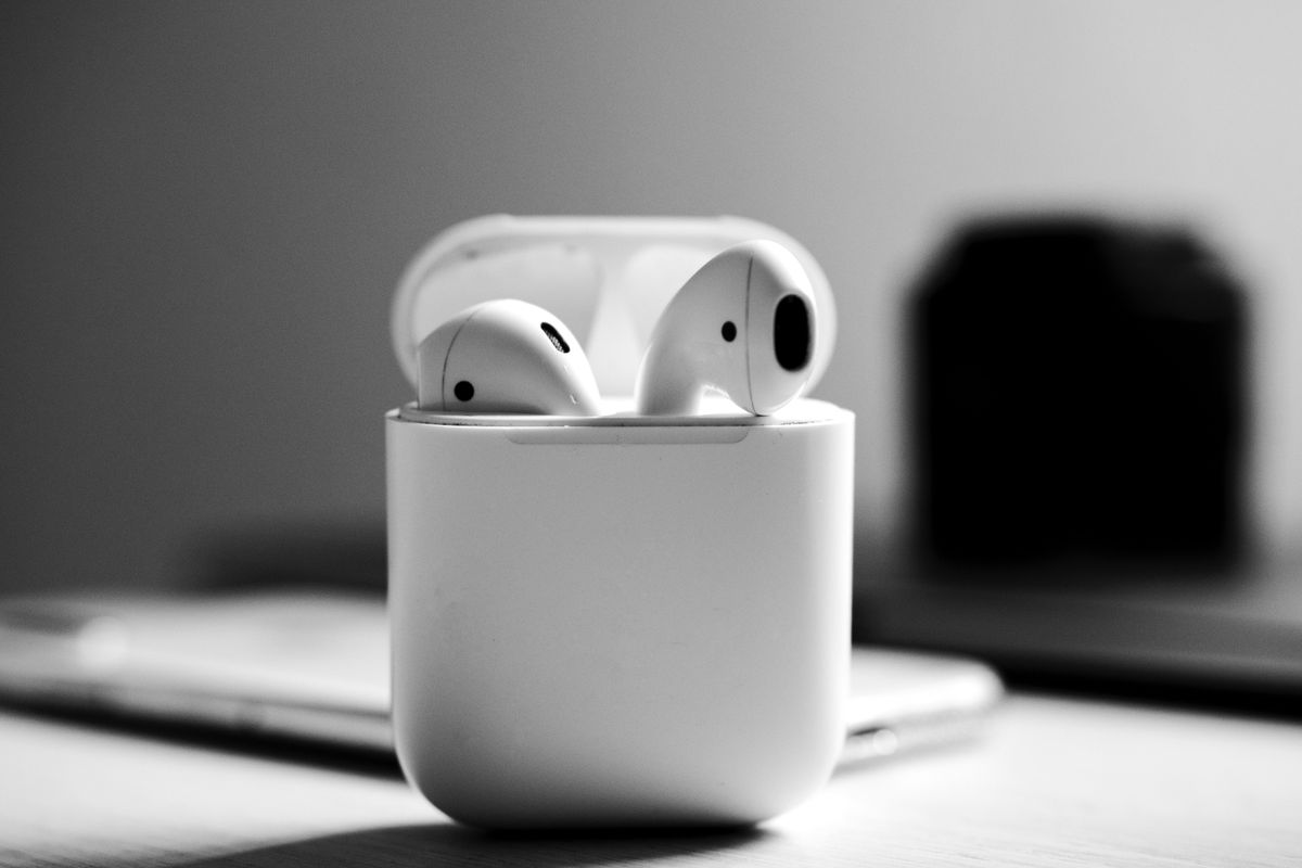 Monochrome close-up shot of wireless earbuds in an open charging case on a table.