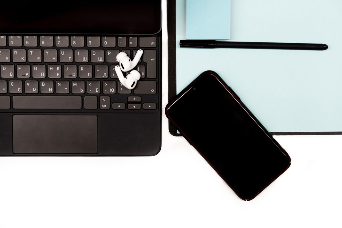 Close-up of a workspace featuring a laptop, smartphone, and wireless earbuds on a desk.