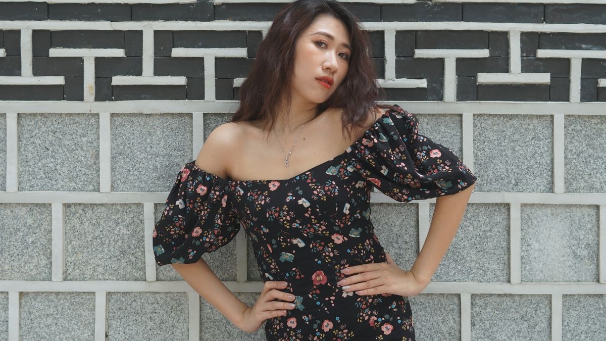 Young woman in floral-patterned dress posing confidently against a textured wall.