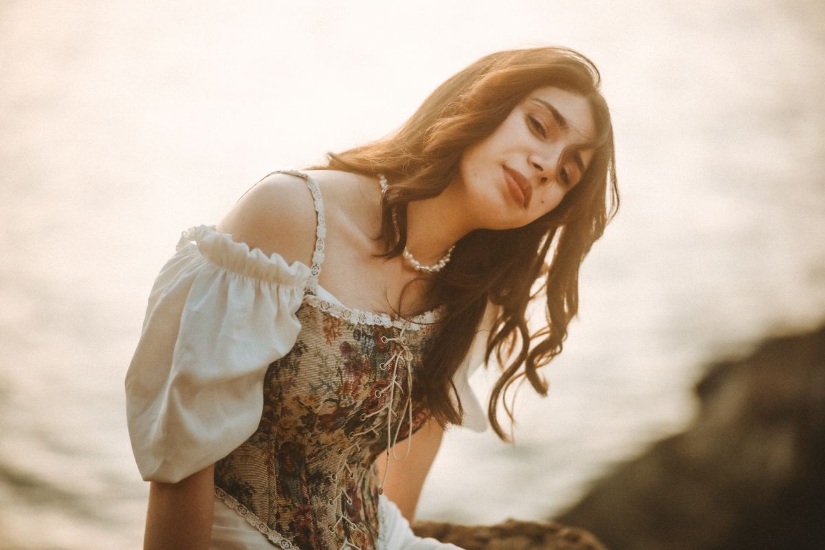 A contemplative woman in a floral dress reflects by the riverbank during a warm day.