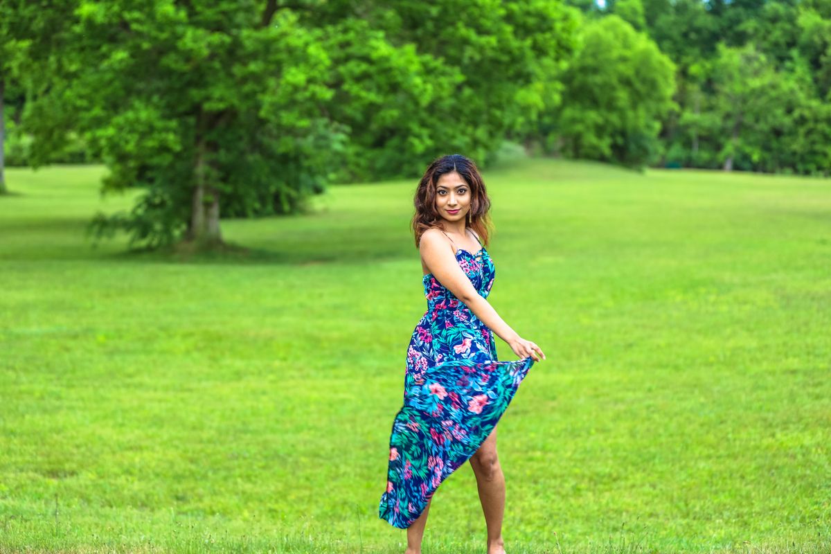 A woman in a floral dress poses gracefully in a green park during summer.