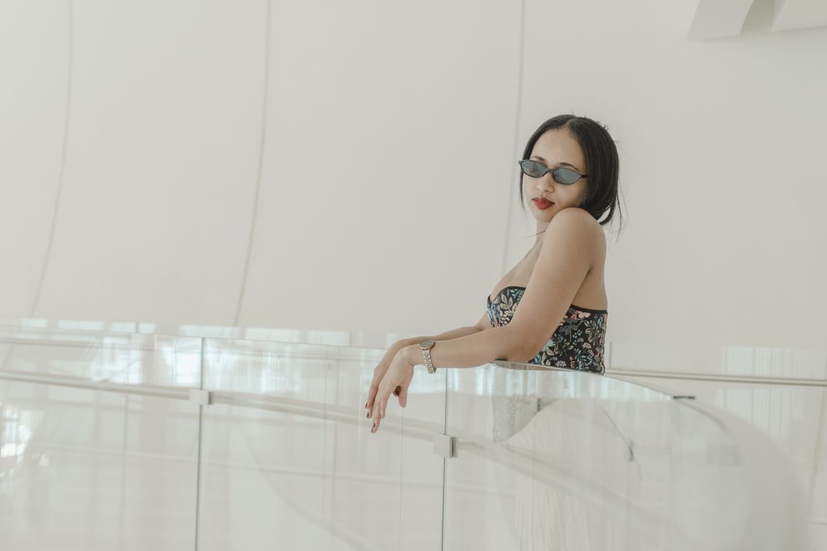 Chic woman in sunglasses and floral dress posing in a sleek modern indoor setting.