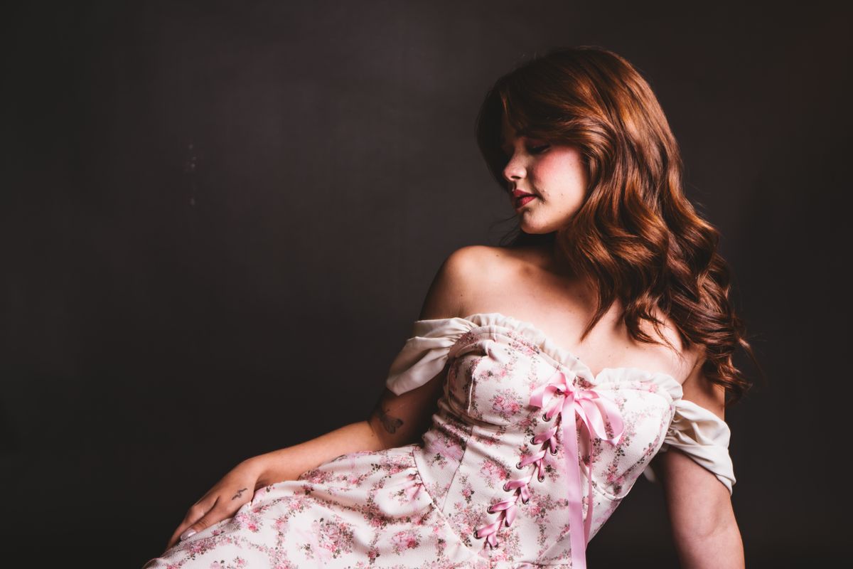 Chic portrait of a woman in a floral corset-style dress against a dark backdrop.