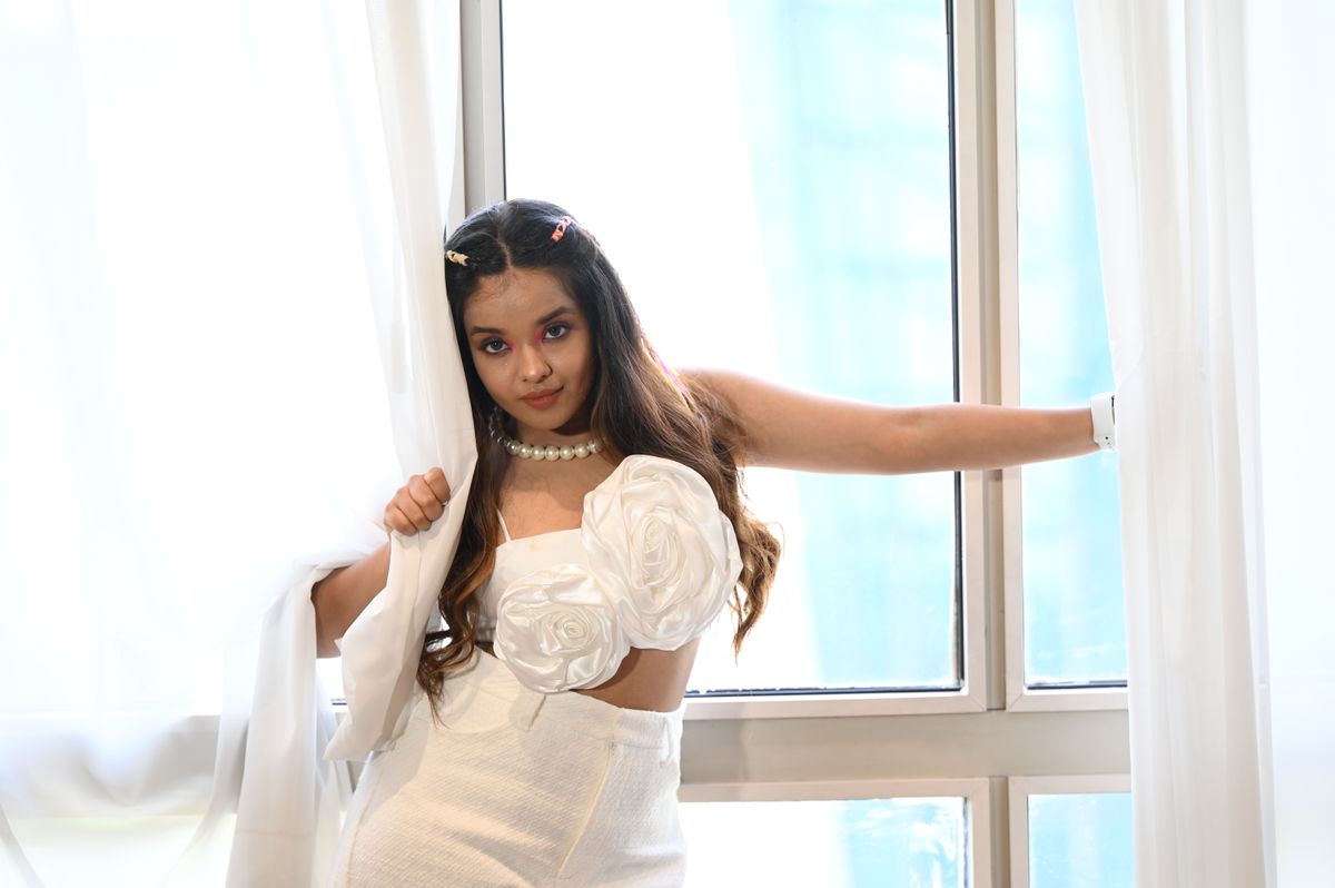 Young woman in white dress posing gracefully by a sunlit window with curtains.