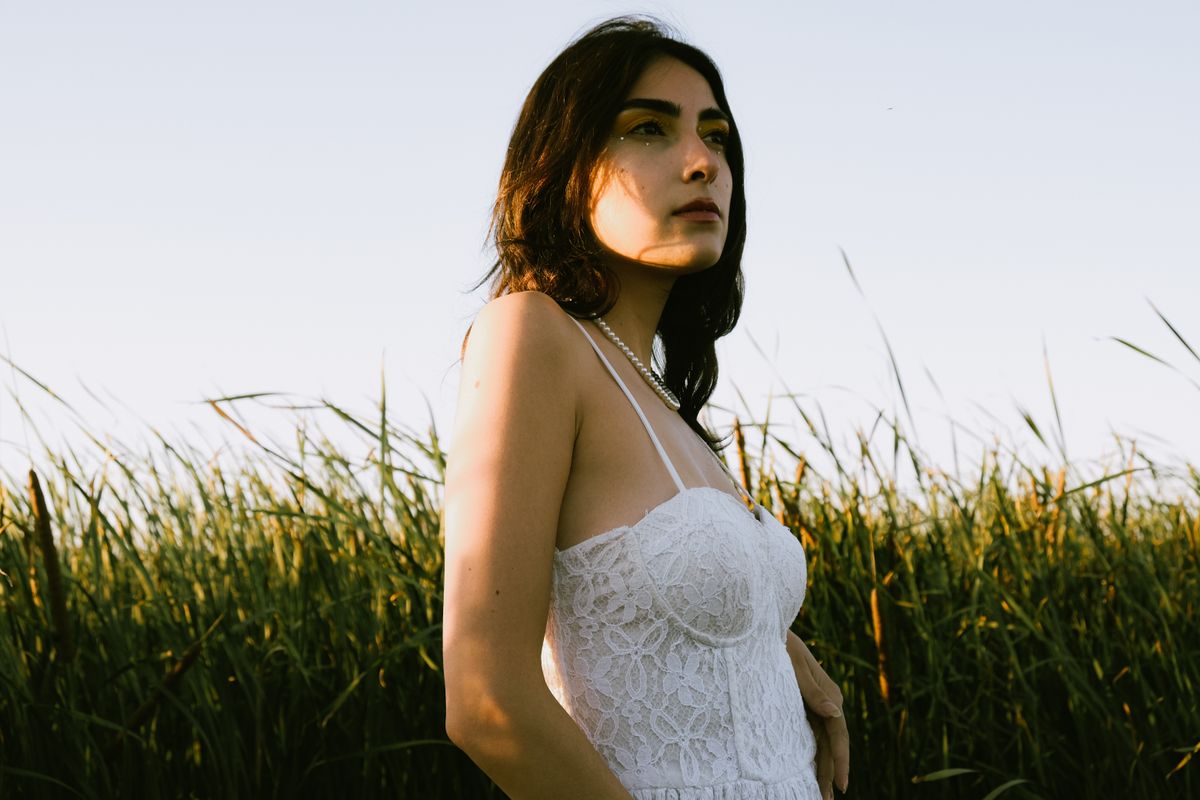 Young woman in a white lace dress posing in a natural reeds setting during golden hour.