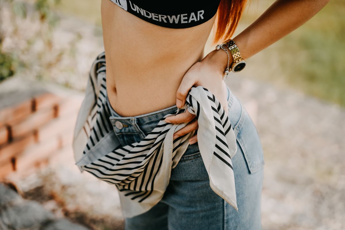Close-up of a woman's fashion posing with scarf and jeans outdoors.