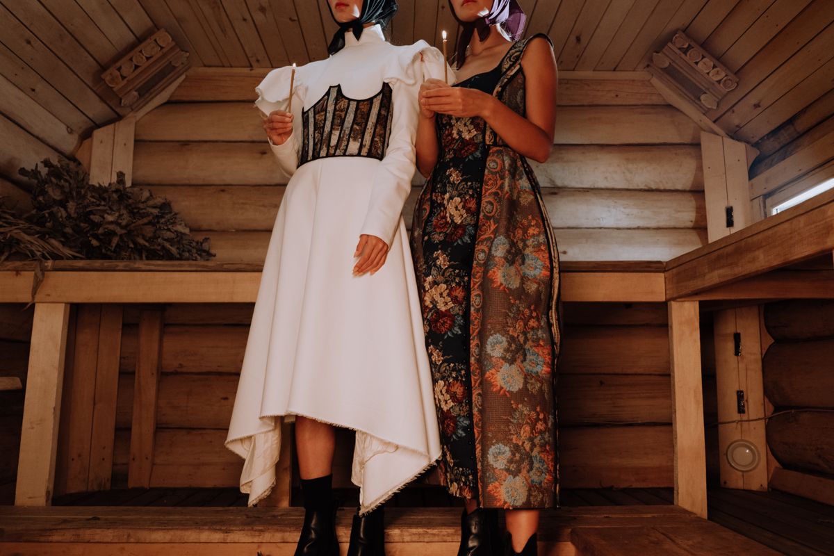Two models in vintage dresses posed in a rustic wooden setting, embodying modern fashion style.