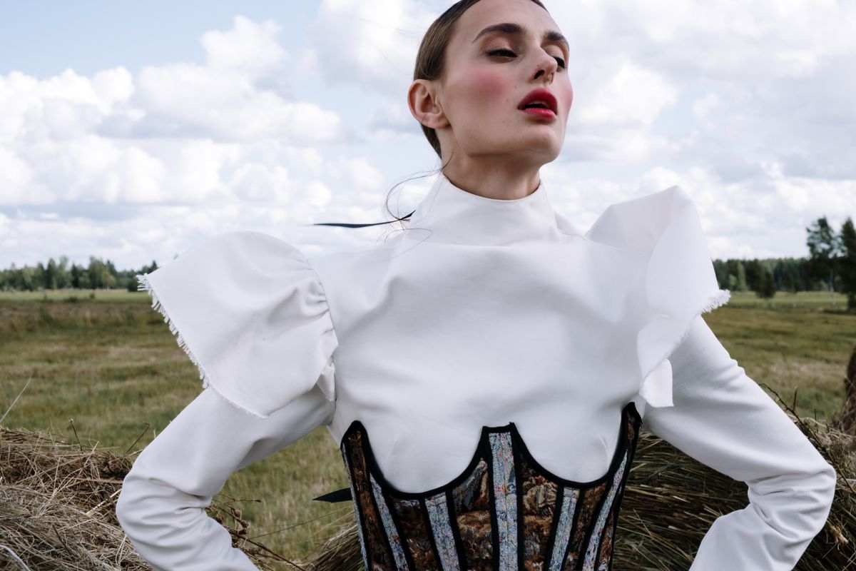 Portrait of a woman in a stylish vintage outfit in a field under a bright sky.