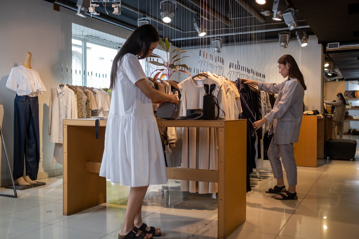 Two women browsing clothes in a modern indoor fashion store.