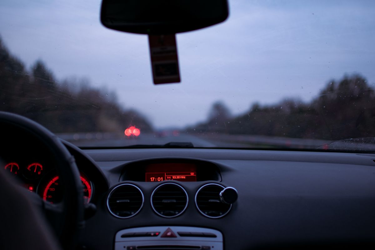 Car dashboard and windshield view on a highway at twilight with illuminated dials and road ahead.