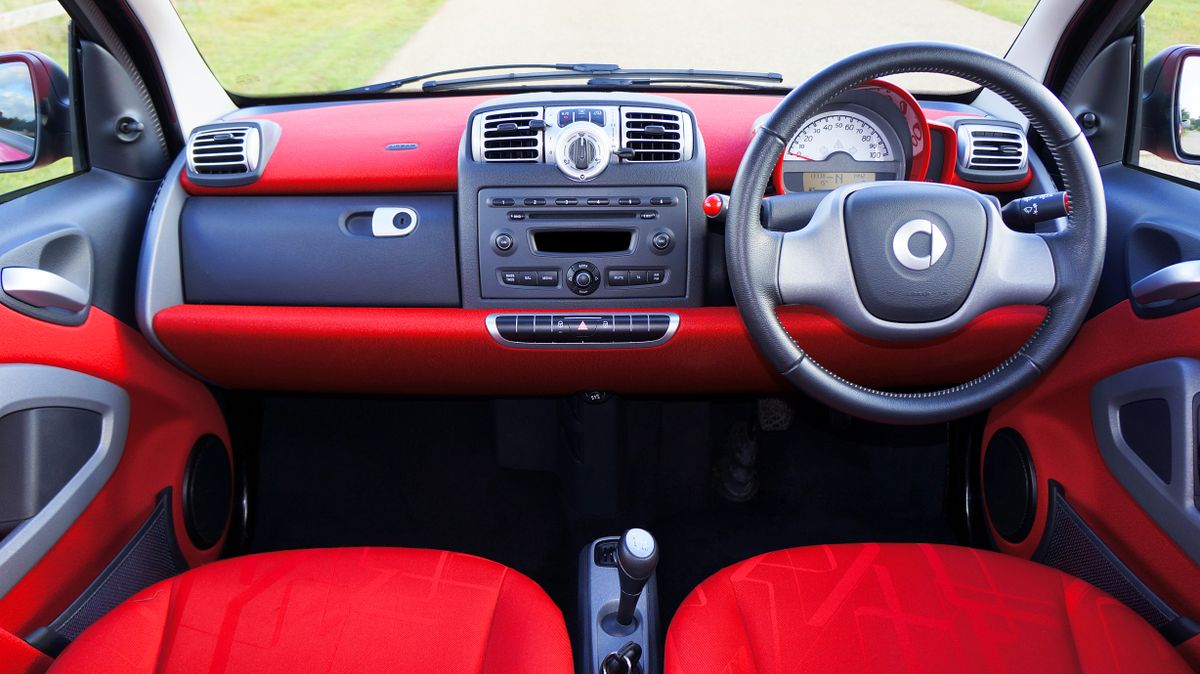 View of a compact car's red interior with a detailed dashboard and steering wheel.