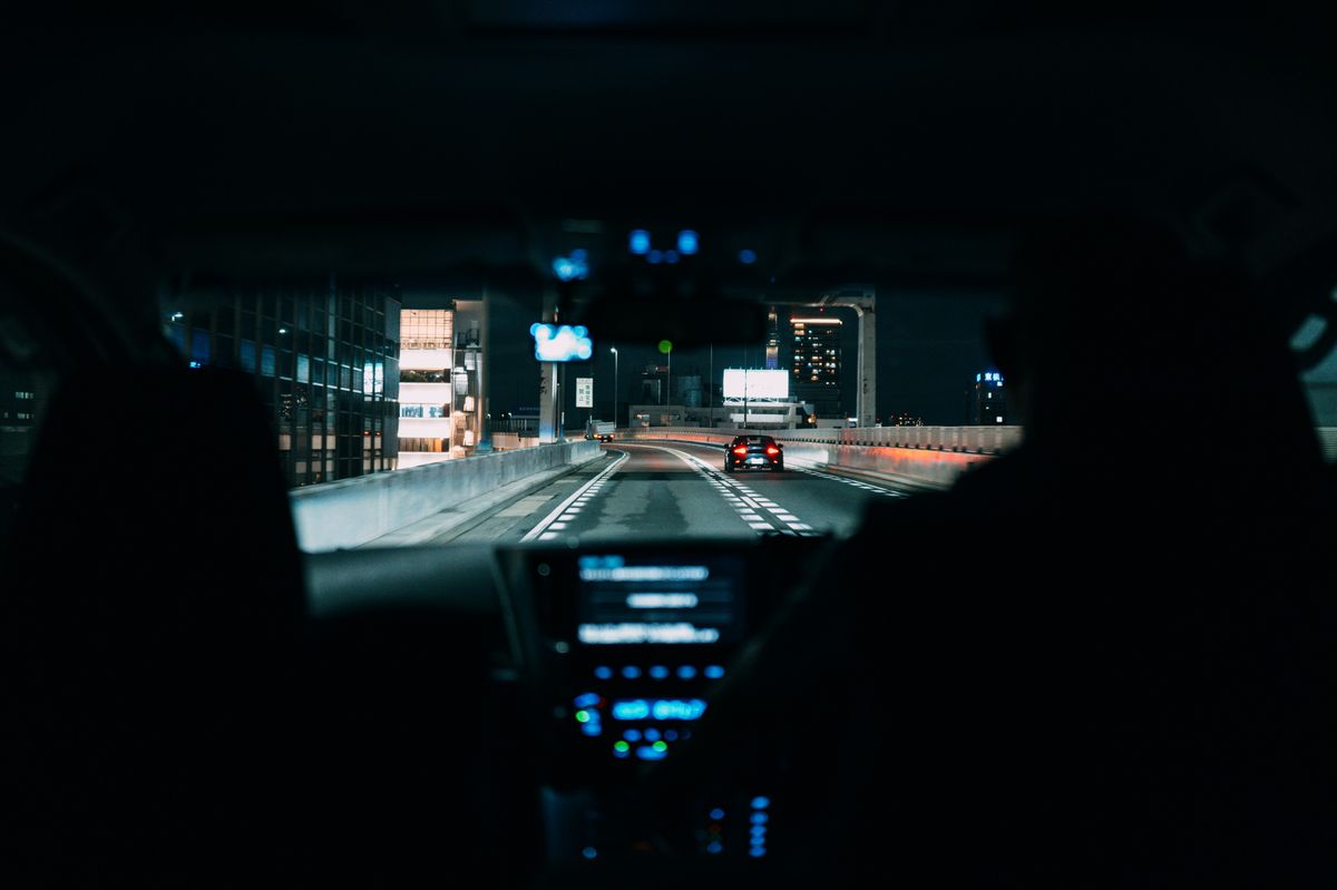View from inside a car driving on a city highway at night, highlighting urban life.