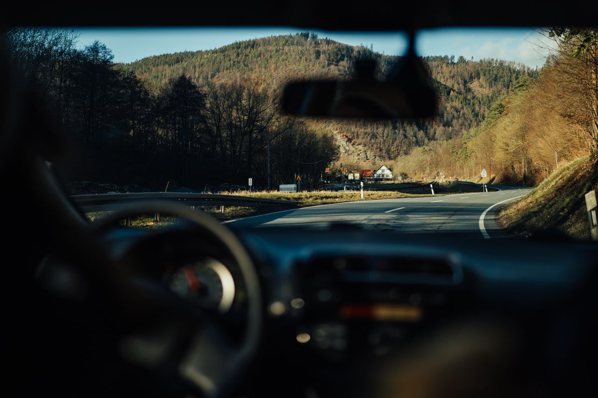 View from car interior of a winding road through scenic mountains and forests.