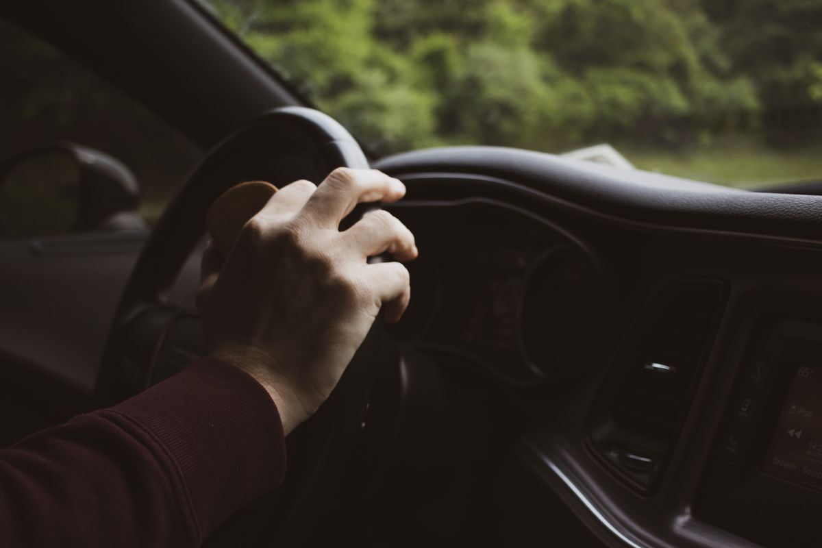 Close-up of a hand on a car steering wheel, depicting a relaxed driving moment.