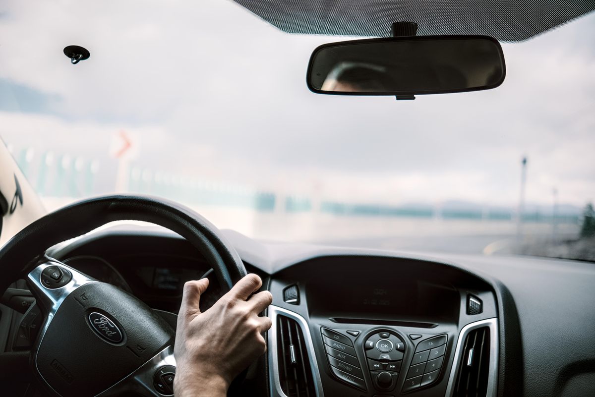View from inside a car showing steering, rear-view mirror, and blurred road outside.