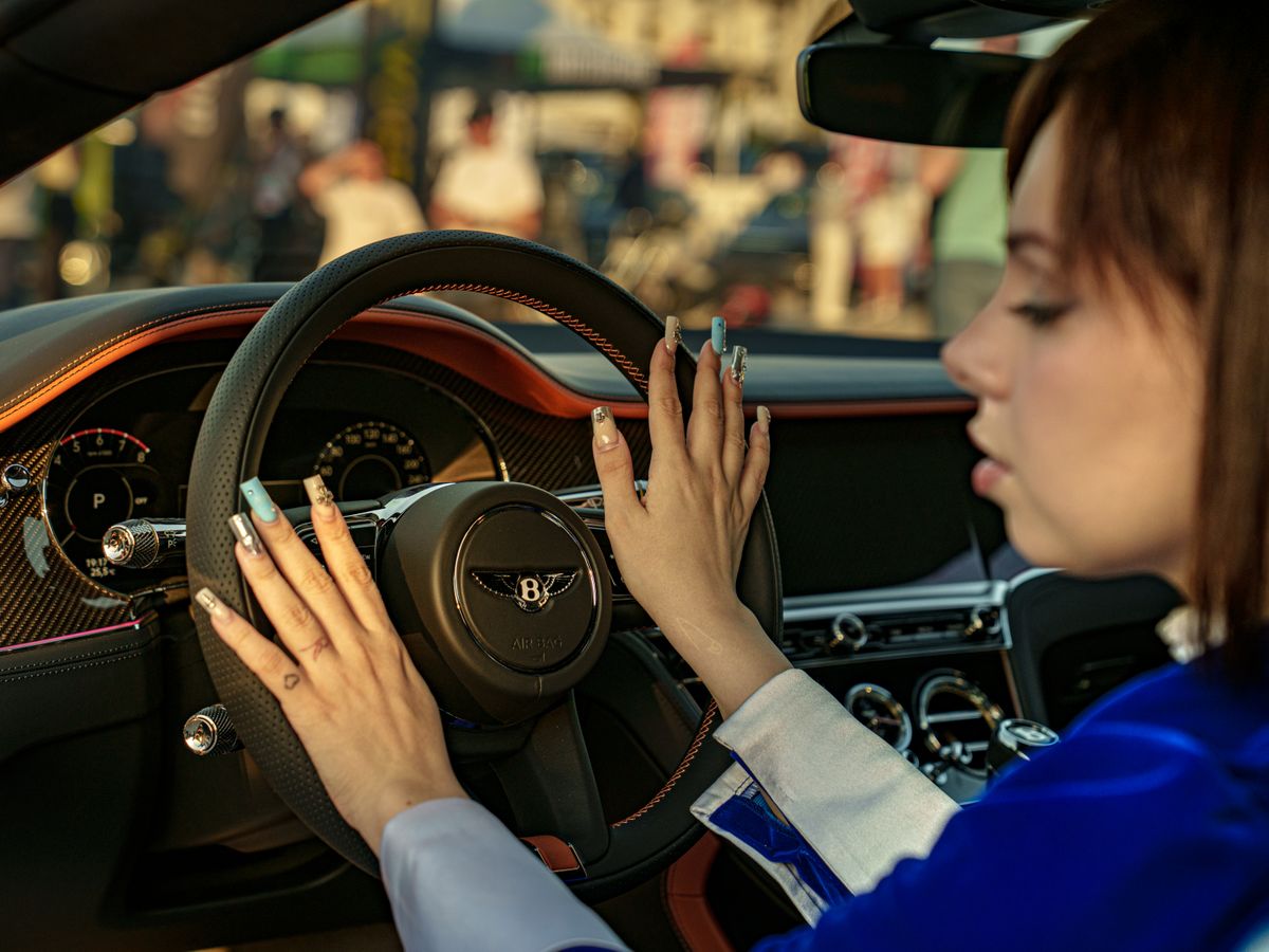 Young woman touching steering wheel of luxury car interior, depicting elegance and sophistication.