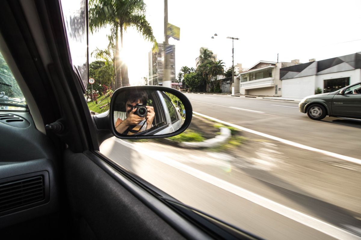 Photographer captures journey reflection on the road in a car side mirror.