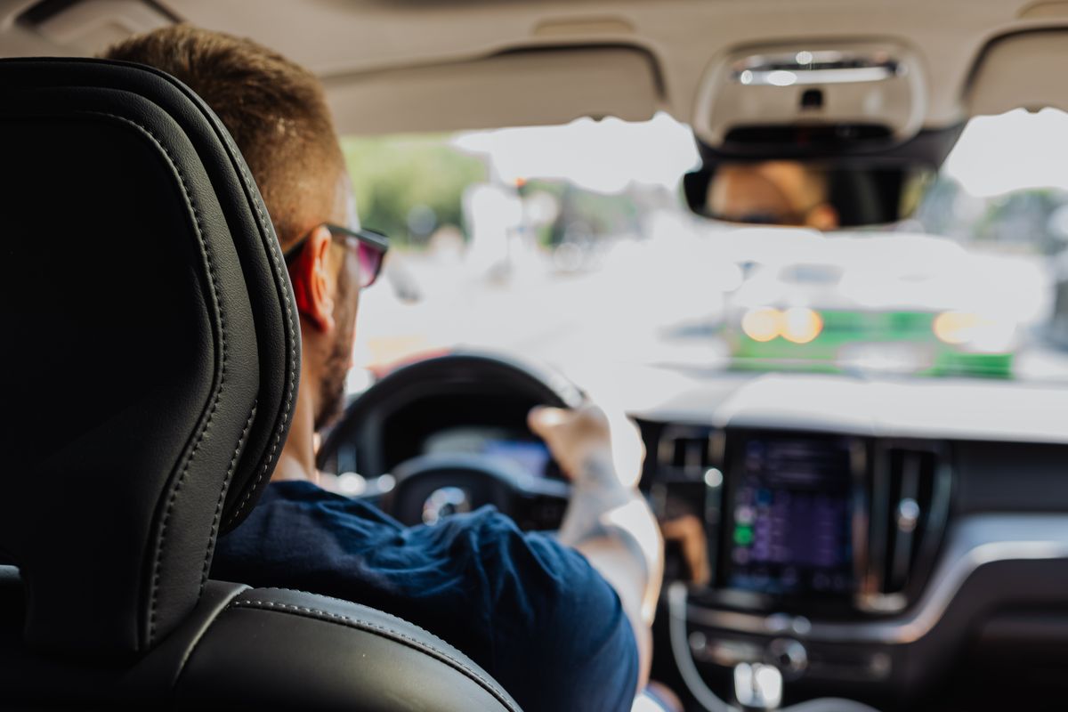 Close-up of a man driving a modern vehicle from behind with a blurred urban background.