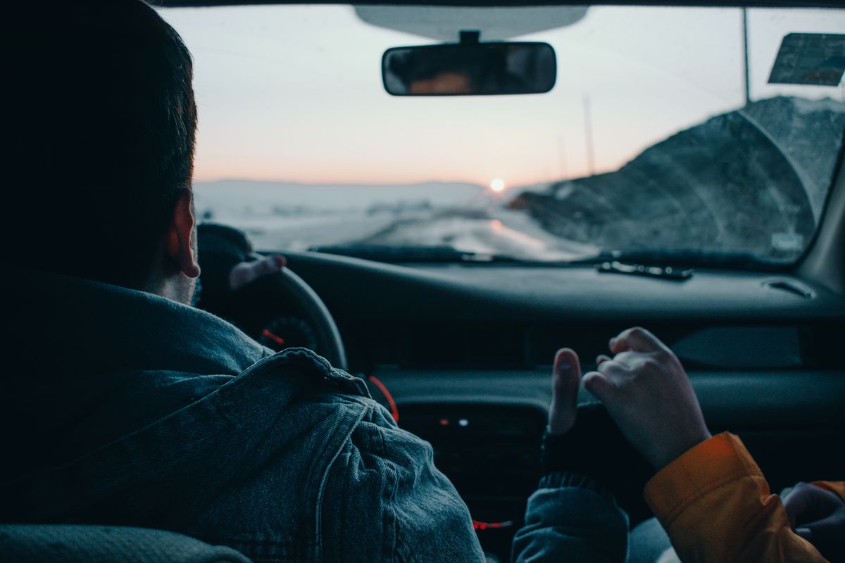 Back view of crop anonymous couple of travelers driving modern automobile along asphalt road at sunset