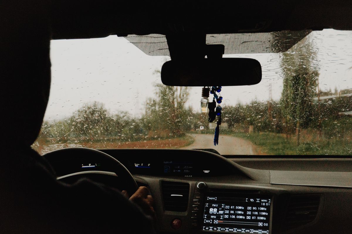 Driving through a scenic road in the rain, capturing the view from inside the car with raindrops on the windshield.