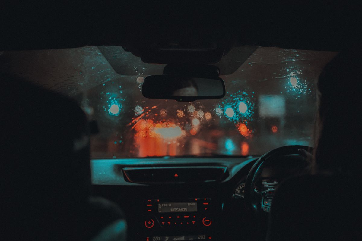 A cinematic view from inside a car driving through rainy Manchester at night with neon lights.