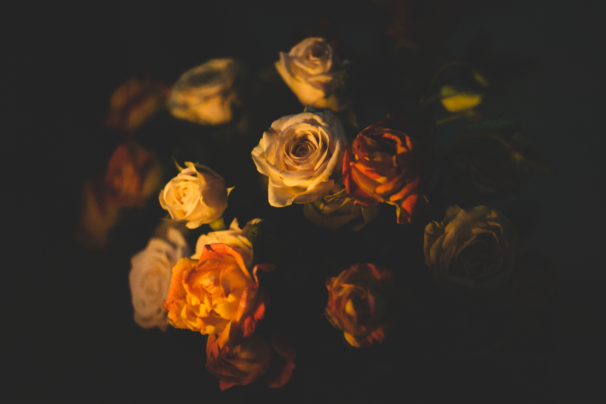 A dark and dramatic floral arrangement with various colored roses in a dim setting.