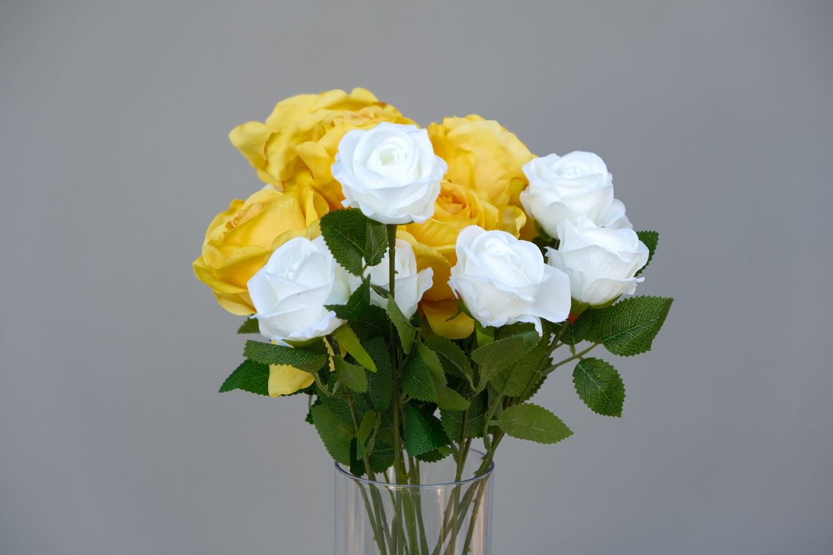 Bouquet of yellow and white roses arranged in a clear glass vase against neutral background.