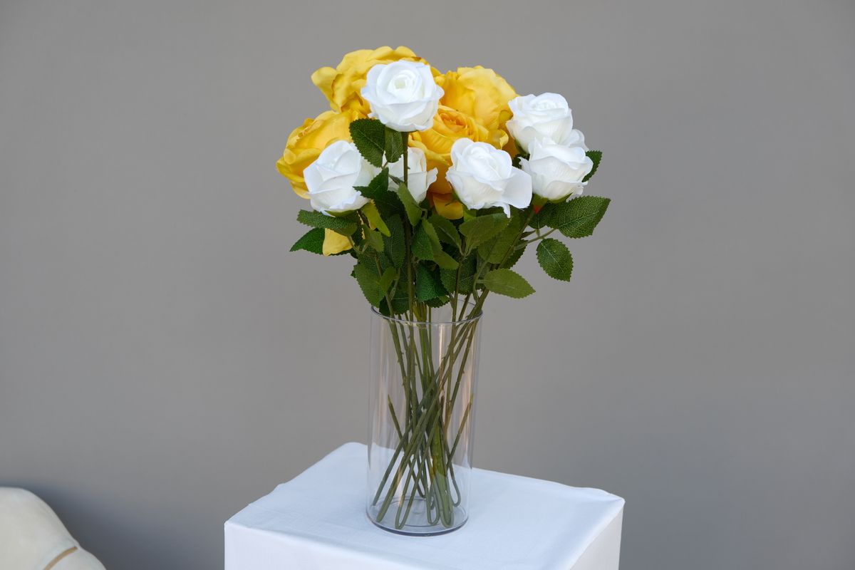 A beautifully arranged bouquet of yellow and white roses in a clear glass vase against a neutral background.