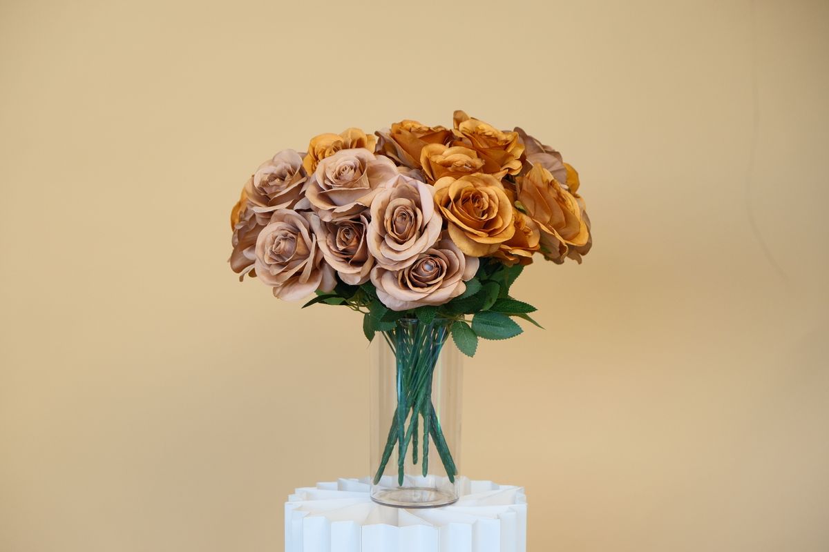Aesthetic arrangement of brown roses in a glass vase on a neutral background.