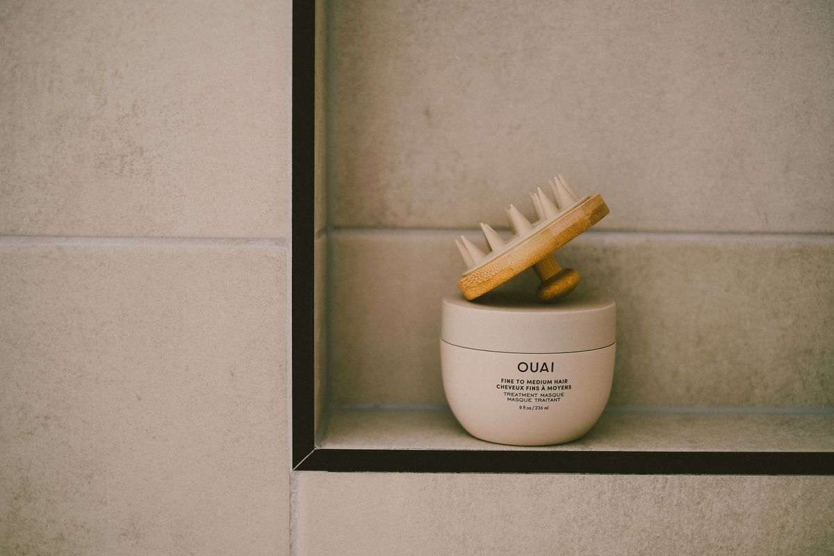 Elegant bathroom shelf featuring OUAI hair mask and massage brush on neutral tiles for a modern self-care setting.
