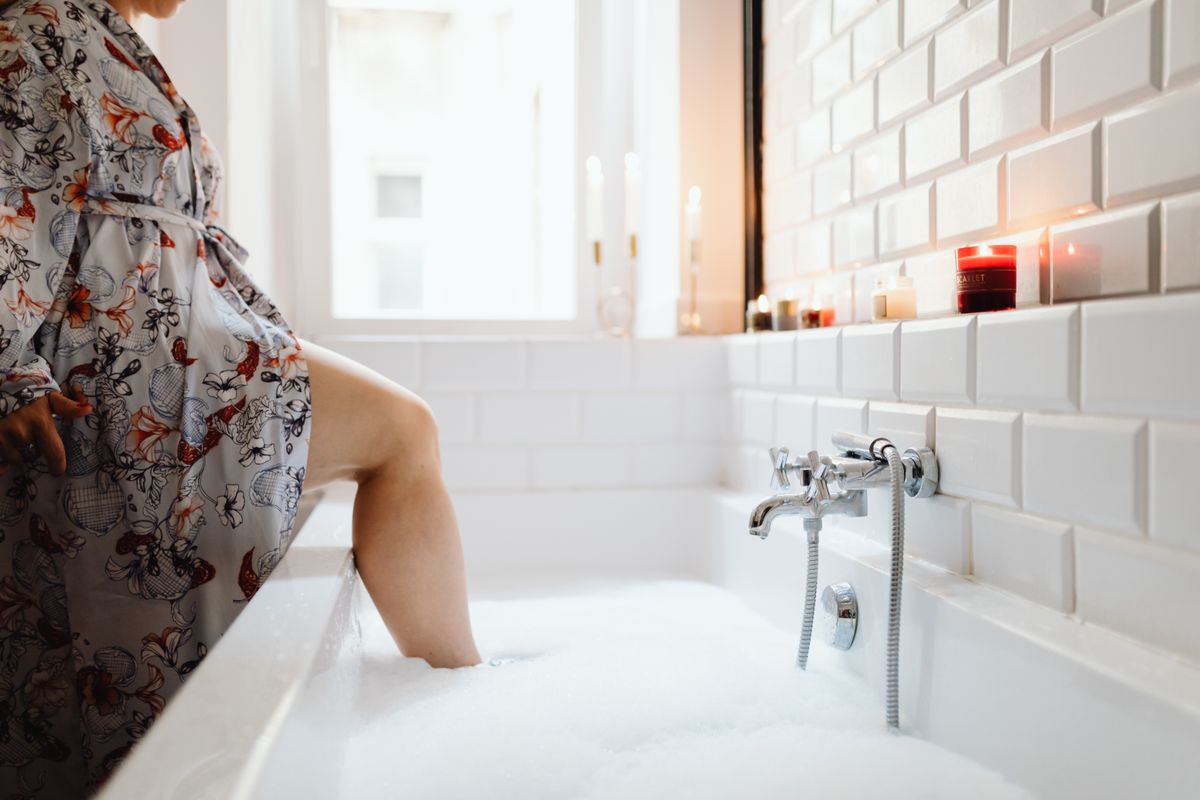 A serene bathroom scene with a person stepping into a bubble bath surrounded by candles.