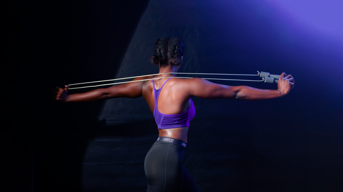 Back view of woman using a jump rope during workout, emphasizing fitness and strength.