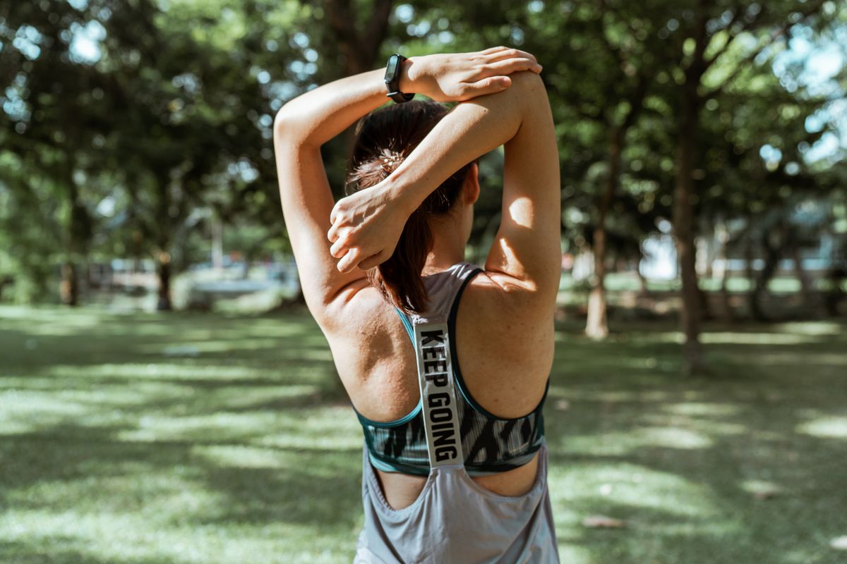 Back view of anonymous sportswoman in activewear doing stretching exercise for back and arms alone in park