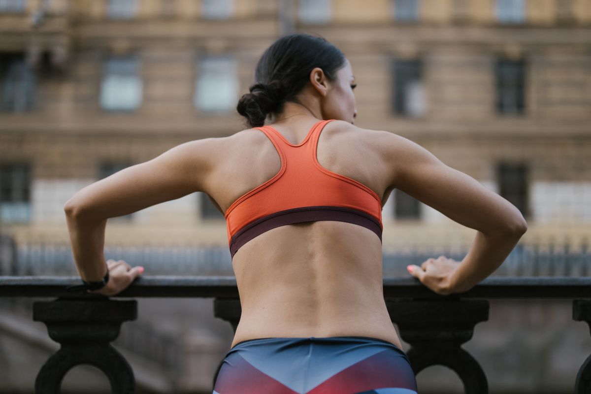 Back view of a woman in activewear working out outdoors on a balcony.