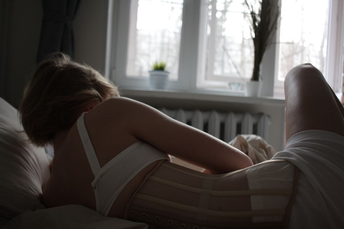 Woman lying in bed wearing a corset, with soft window light creating a peaceful mood.